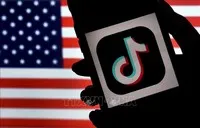 Biểu tượng ứng dụng TikTok trên màn hình điện thoại và quốc kỳ Mỹ (phía sau). Ảnh: AFP/TTXVN